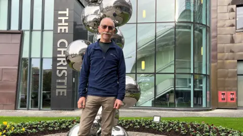 Photograph of patient Richard Nelson, who has received a new type of vaccine for bowel cancer. He's pictured outside the Christie Hospital.