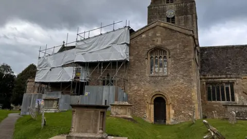 Darrell Jacobs The front of st mary's church, with one portion covered by scaffolding and white covering. In front of the church is a garveyard.