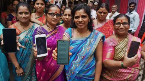 Women who were beneficiaries of a government cash transfer scheme showing their bank passbooks and the message of the scheme money received on their mobile phones in Maharashtra, India - 2024. 