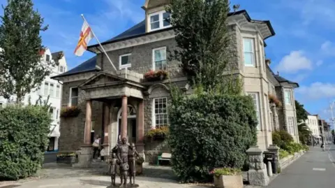 A picture of the front of what is due to be the Victor Hugo Centre. It is a large brick building with a statue outside the front of it. 