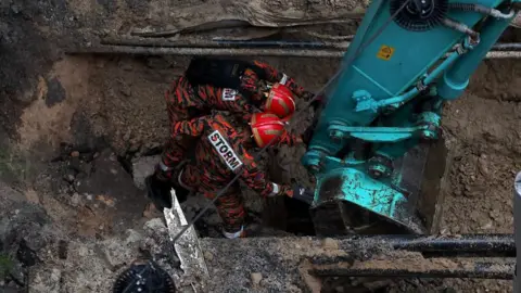 EPA Malaysia Fire and Rescue Department officers inspect the site where a woman fell into an 8m deep sinkhole in Kuala Lumpur