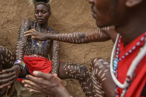 GERALD ANDERSON/GETTY IMAGES Two Maasai wearing their traditional attire. One man is helping the other apply body art.