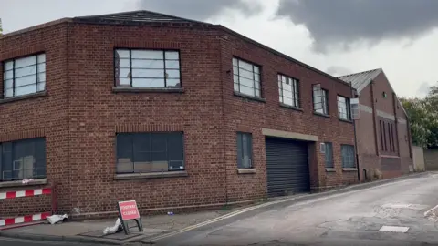 Connor Bennett/BBC The museum store room on Charles Street. It is a red brick building across two storeys. Some of the windows have been boarded up while others have been opened. The pavement has been cordoned off.