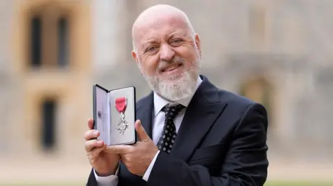 PA Media A close up picture of Bill Bailey holding up his MBE
