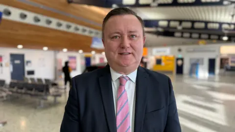 Richard Thomasson - a man wearing a suit and tie standing inside Guernsey Airport.