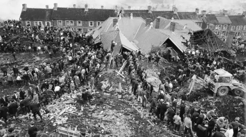 Getty Images Black and white image of lines of villagers and emergency services helping to free trapped children and adults