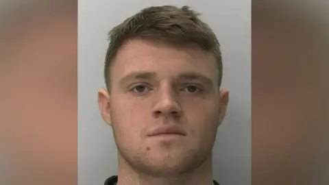 Police mugshot of Joseph Jones. He has short brown hair and stubble on his lower face.