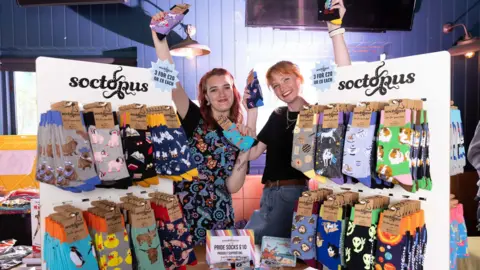 Socktopus Two women stand in a shop surrounded by unique, brightly coloured socks. They both have red hair.