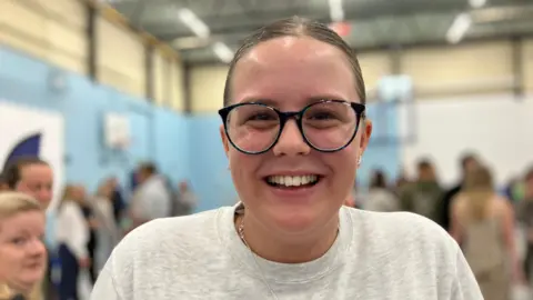 Launceston College pupil Josie smiling at the camera. She has a light grey T-shirt on with a silver necklace and black-rimmed glasses