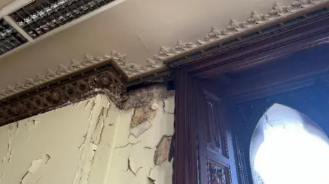 Mole Valley District Council Cracked plaster on the walls of the interior of Pippbrook House, with cracks extending to the wooden cornice and gothic window frames.
