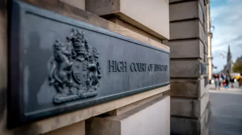 PA Media A black sign for the high court on a light sandstone with a coat of arms on the near side.