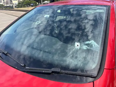 A bullet hole in the windshield of a red car parked at Bondi.