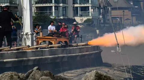 Cowes Week Martin Allen A ceremonial cannon is fired from the waterfront as spectators watch from nearby.