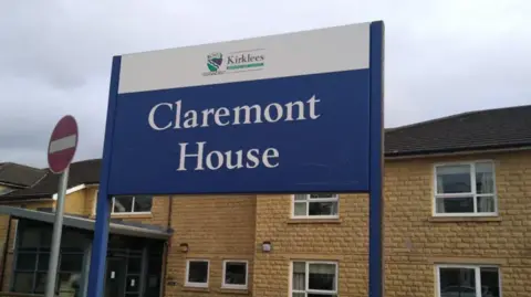 Image shows a two storey sand coloured building. With a blue and white sign.