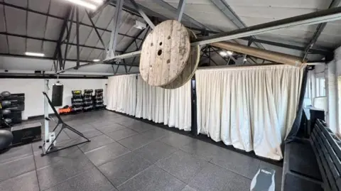 Chloe Cartwright A large ceiling to floor white curtain is drawn across half the gym. 