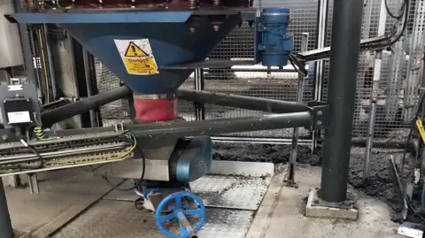 HSE A piece of machinery - a surge hopper - with a warning sign on it.