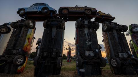An image taken from ground level shows Carhenge at sunrise during the 2023 solstice 