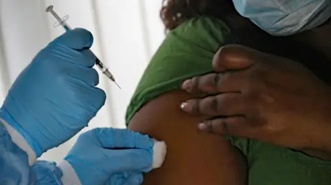 A medical professional wearing blue gloves administers an injection into a woman's arm.