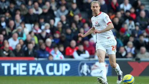 Getty Images Chadwick, in a full white MK Dons kit, passing the ball.