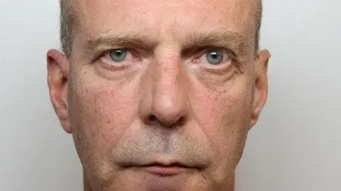 A mugshot of Colin Lomas, who is balding with grey hair on the sides and has greyish blue eyes.