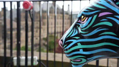 A decorated lion sculpture with blue and purple stripes is situated infront of black railing