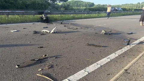 A smoking engine is resting up against the central reservation with debris scattered across the road.