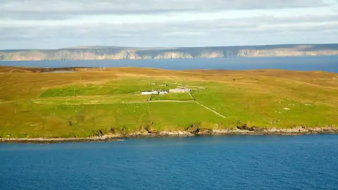 Getty Images A view across the island of Yell with a small farmhouse and water surrounding it and another land mass in the distance.