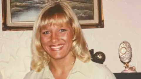 Family photo Chantel Taylor has blonde hair and is wearing a cream blouse and is smiling at the camera.