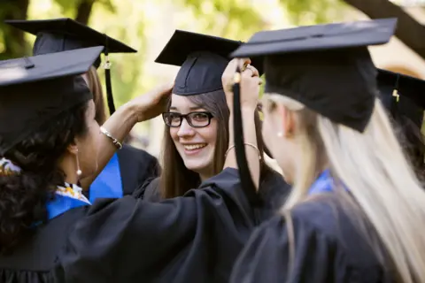 Getty Images Three young women in university graduation caps and gowns - one woman adjusts the caps of her friends.