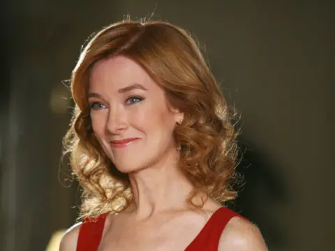 Getty Images Valerie Mahaffey is wearing a red dress. the image is cropped to her head and shoulders. her hair is red and curled.