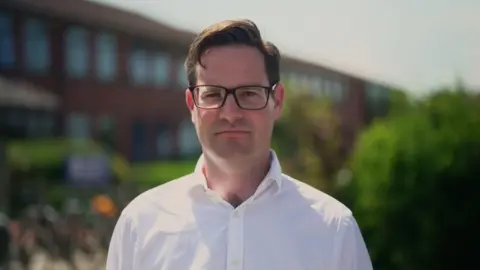 Gemma Laister / BBC Nick Wakeling, a teacher at Colyton Grammar School, is wearing glasses and a white shirt and looks straight at the camera. 