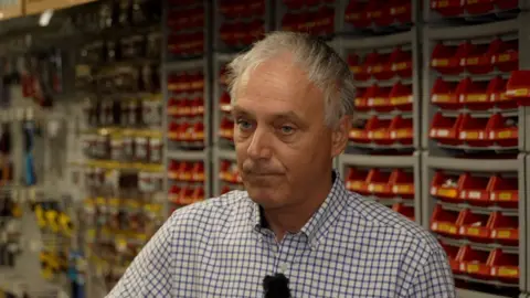 Toby Roberts, owner of D&G Hardware store in Alresford standing in front of shelves of nails.