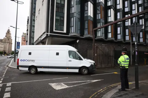 PA Media A white van turns into a road as a policeman stands watch