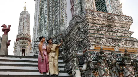 Getty Images گردشگران با لباس‌های سنتی تایلندی در معبد Wat Arun در روز Vesak در بانکوک، تایلند، در 22 مه 2024 سلفی می‌گیرند. 