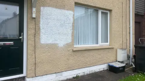 A house with graffiti daubed on a wall which has been painted over