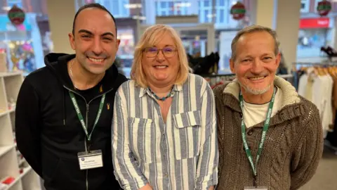 Three people standing in a charity shop in Clacton-on-Sea.