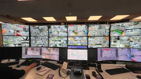 SIMON DEDMAN/BBC A control room with a dozen big TV screens with several CCTV cameras on show.