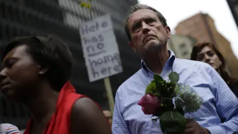 AFP a man holding flowers in front of a sign that reads "Hate has no home here"