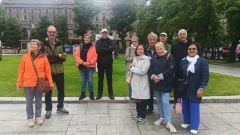 A group of 11 men and women stand in the grounds of Belfast City Hall 