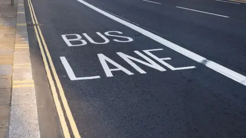 A bus lane with double yellow markings on the side of the road and dark tarmac