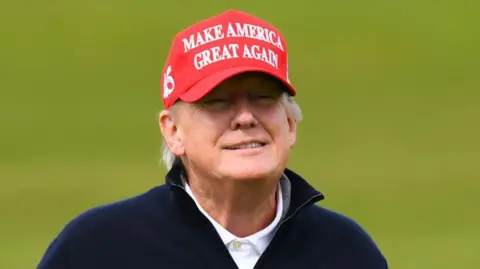 Getty Images Donald Trump on a golf course wearing a navy blue zipper, a white polo shirt and a red cap with the slogan "make American great again"