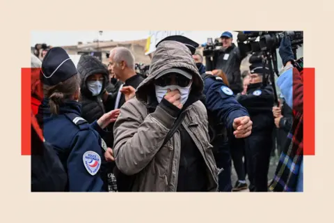 Getty Images A defendant in a mask walks through a crowd of journalists