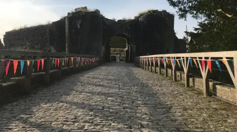 FRIDAY - Lengthening evening shadows of a balustrade are cast across the cobbles on an entrance to the ruins of Corfe Castle with colourful bunting hanging from each side