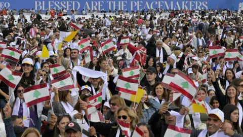 EPA A crowd waves Lebanese and Vatican flags during a Mass celebrated by Pope Leo XIV on the Beirut waterfront, in Lebanon (2 December 2025)