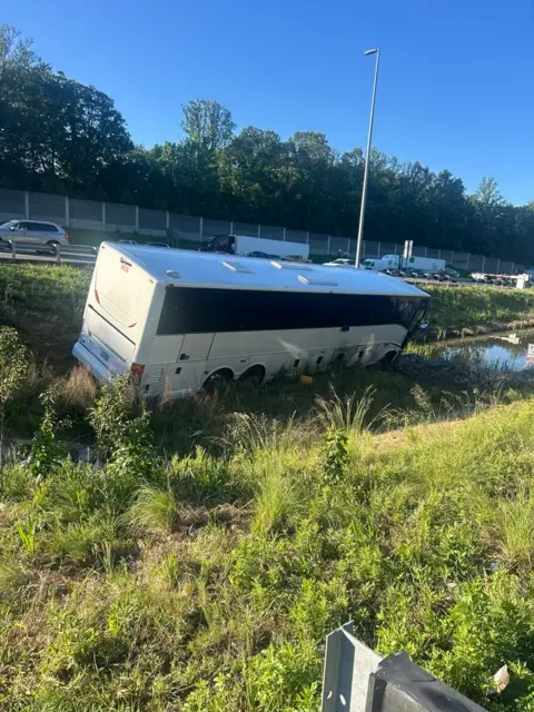 Virginia State Police A white and black bus sits on greenery on the side of a road after a crash.