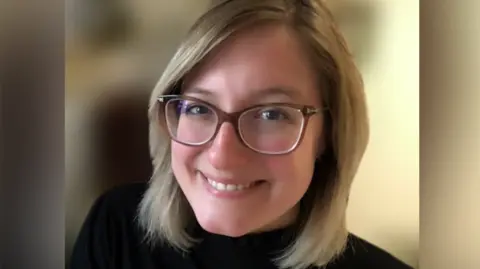 Veronica Lamarche Dr Veronica Lamarche smiles at the camera. She has a blonde bob and wears glasses and a black top. The background behind her has been blurred. 