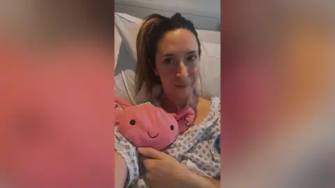 Claire Lyness Gynaecology patient Claire lies in her hospital bed after surgery with a womb-shaped toy as her mascot.