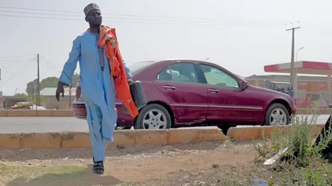 Professor Kabir Abu Bilal walking by his car in Zaria, Nigeria - December 2023