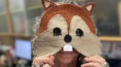 A staff member at Acorn is holding up a home made fabric face mask of a red squirrel to wear for the event.