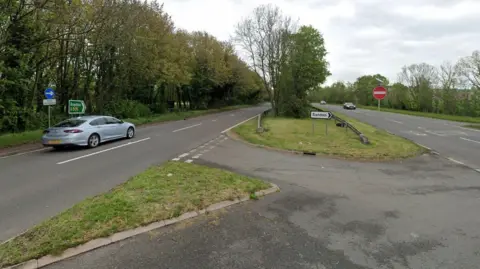 The A505 Baldock bypass, showing three car, several road signs, including a sign to Sandon, Royston and a central reservation with grass and trees in the area 